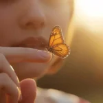 A person softly holding a butterfly on their fingers with warm natural lighting and an aesthetic romantic vibe.